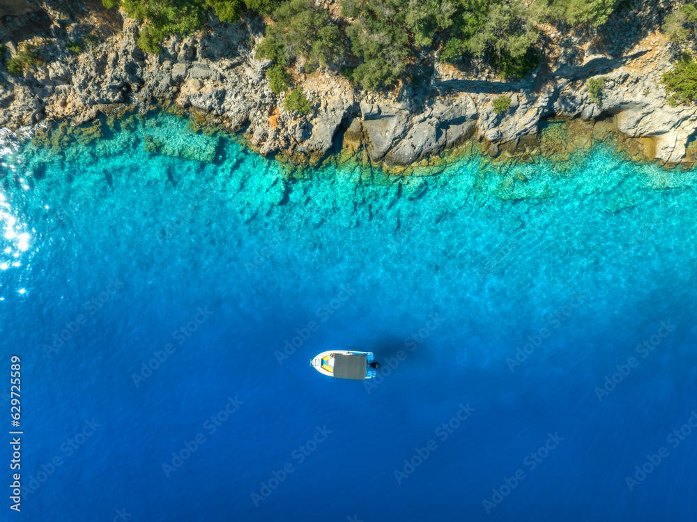 Aerial view of alone small motorboat on the sea in summer sunny day. Oludeniz, Turkey. Top drone view of bay, yacht, sailboats, transparent blue water, sand, stones and green forest. Travel. Boat
