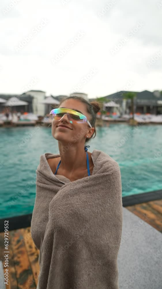 Wrapped in a towel, a lovely young woman dances near the pool, trying to stay warm in the bad weather and rain. Wrapped in a towel, a lovely young woman dances near the pool, trying to stay warm in the bad weather and rain.