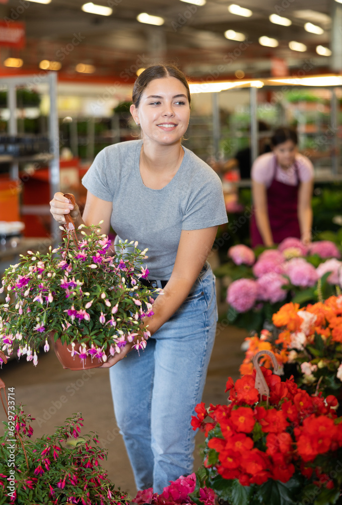 Smiling young woman customer choosing fuchsia in flower-pot in open-air plants market