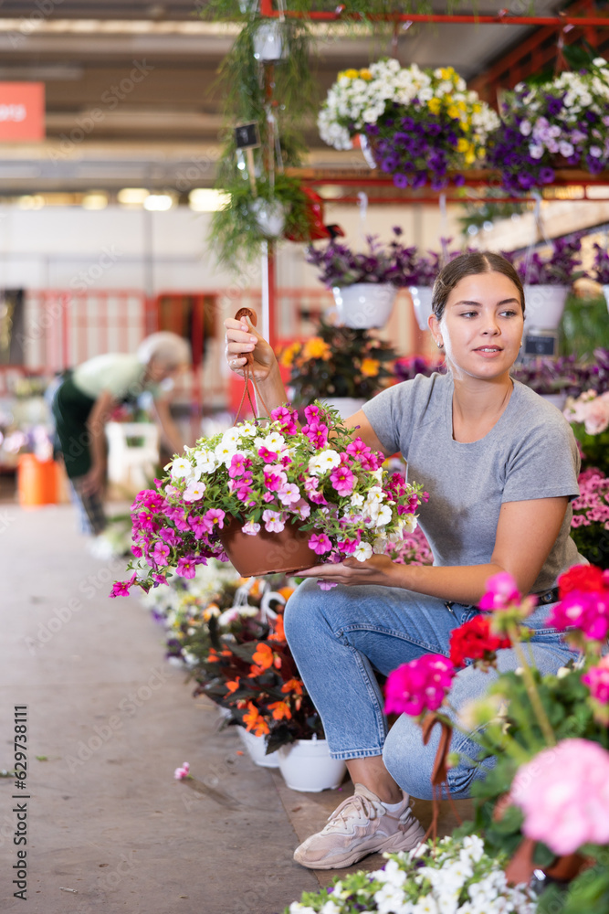 Pleased young woman customer choosing calibrachoa in flower-pots in open-air plants market