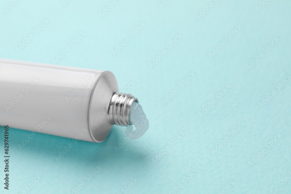 Naklejka premium Open tube of ointment on light blue background, closeup. Space for text