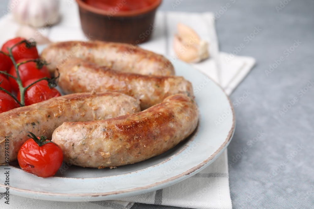 Plate with tasty homemade sausages and tomatoes on grey textured table, closeup. Space for text Plate with tasty homemade sausages and tomatoes on grey textured table, closeup. Space for text