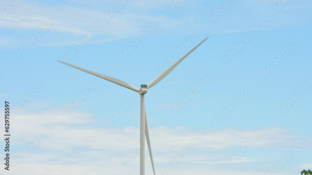 Windmills farm generating green energy. Large wind turbine with blades in the field, below view. Sustainable alternative energy. Slow movement telephoto lens.Blue summer sky. Windmills farm generating green energy. Large wind turbine with blades in the field, below view. Sustainable alternative energy. Slow movement telephoto lens.Blue summer sky.