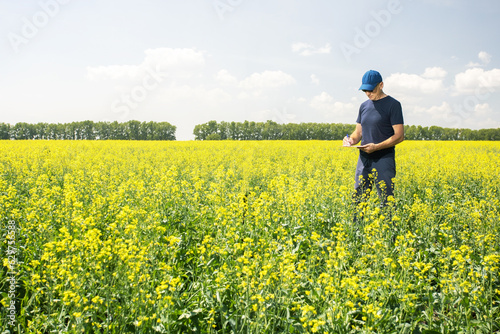 Farmer man standing in rape field with folder in hands and examining the progress of crops.