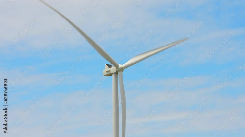 Large wind turbines with blades in the farming fields area, below view. Blue sky. Sustainable alternative energy. Slow movement. Windmills at the farm, generating green energy.