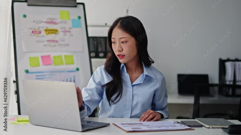 Businesswoman in blue sky shirt is working on laptop and paperwork that show cost planning accounting numbers tables on office space. Businesswoman in blue sky shirt is working on laptop and paperwork that show cost planning accounting numbers tables on office space.