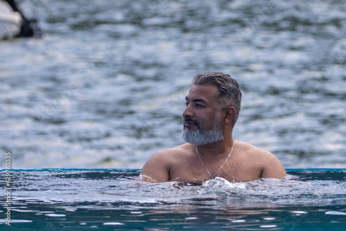 Man with white beard bathing in infinity pool.