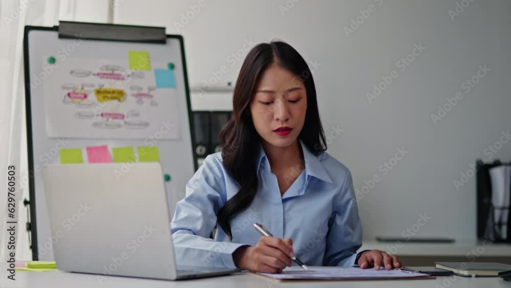 Businesswoman in blue sky shirt is working on laptop and paperwork that show cost planning accounting numbers tables on office space. Businesswoman in blue sky shirt is working on laptop and paperwork that show cost planning accounting numbers tables on office space.