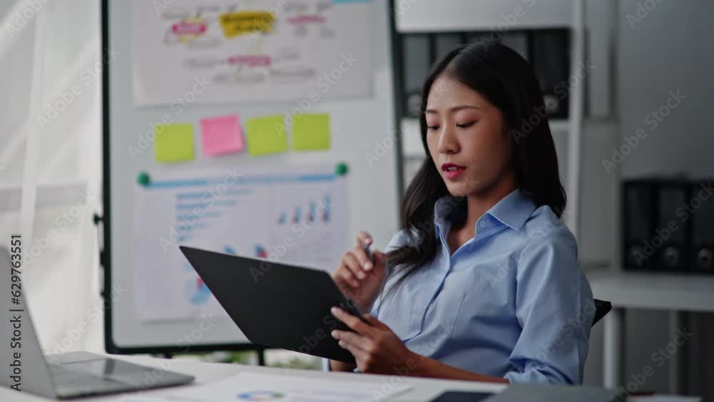 Businesswoman in blue sky shirt is working on laptop and paperwork that show cost planning accounting numbers tables on office space. Businesswoman in blue sky shirt is working on laptop and paperwork that show cost planning accounting numbers tables on office space.