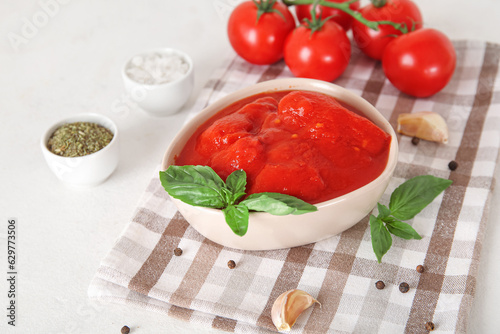Bowl with canned tomatoes and spices on light background
