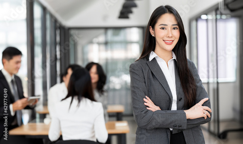 Smiling confident businesswoman looking at camera and standing in an office at team meeting. Portrait of confident businesswoman with colleagues in boardroom.