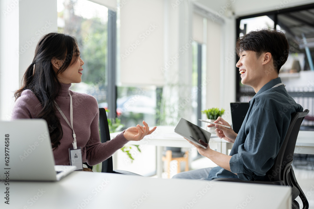 A happy Asian male office worker enjoys discussing work with a female colleague in the office A happy Asian male office worker enjoys discussing work with a female colleague in the office