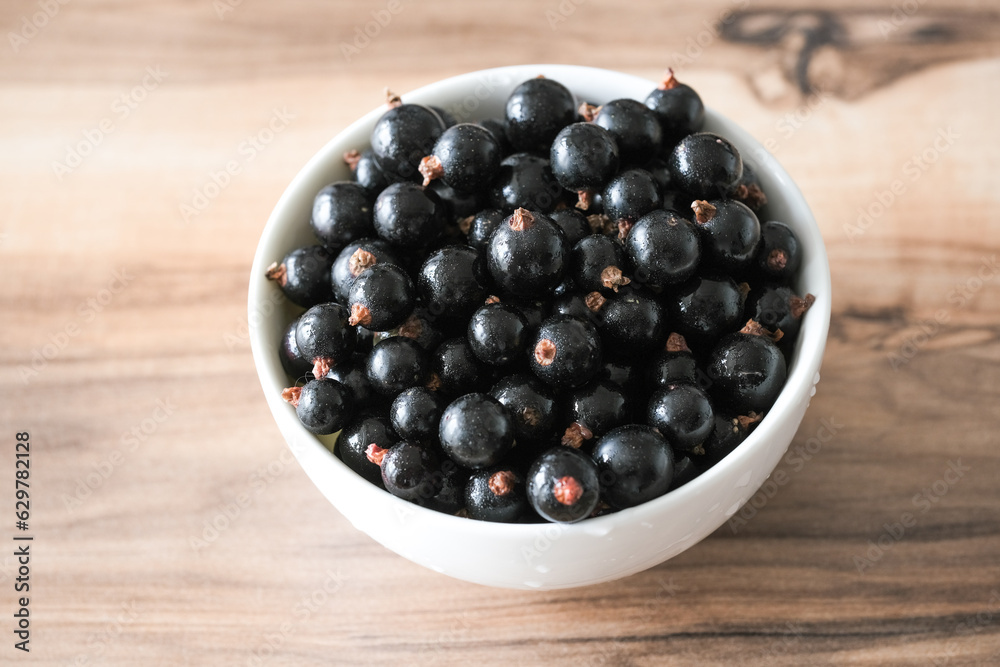 Fresh black currant on in a white bowl. Handful of berries on the wooden table. Fresh black currant on in a white bowl. Handful of berries on the wooden table.