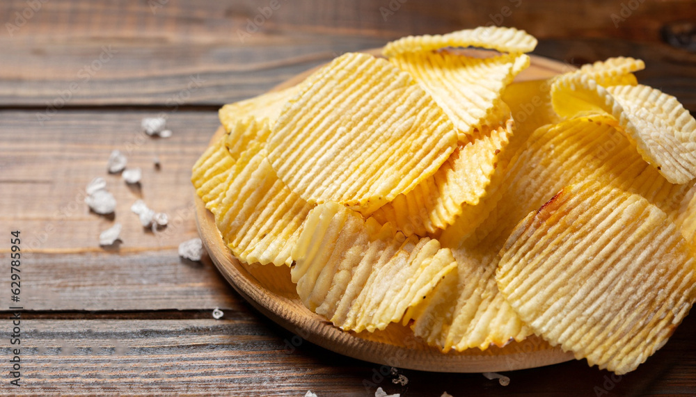 Corrugated potato chips and salt on wooden background. Close up