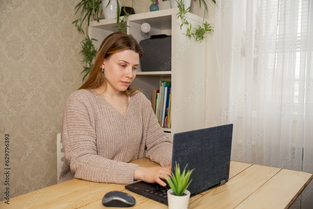 Young woman working with laptop at home. Business woman having a video call with coworker, working online from home at cozy atmosphere. Concept of remote work from home. Distance and remote job.