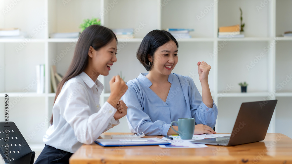 Two asian businesswoman expressing happiness in workplace smiling and raising hands in joy with laptop computer in modern office. Two asian businesswoman expressing happiness in workplace smiling and raising hands in joy with laptop computer in modern office.