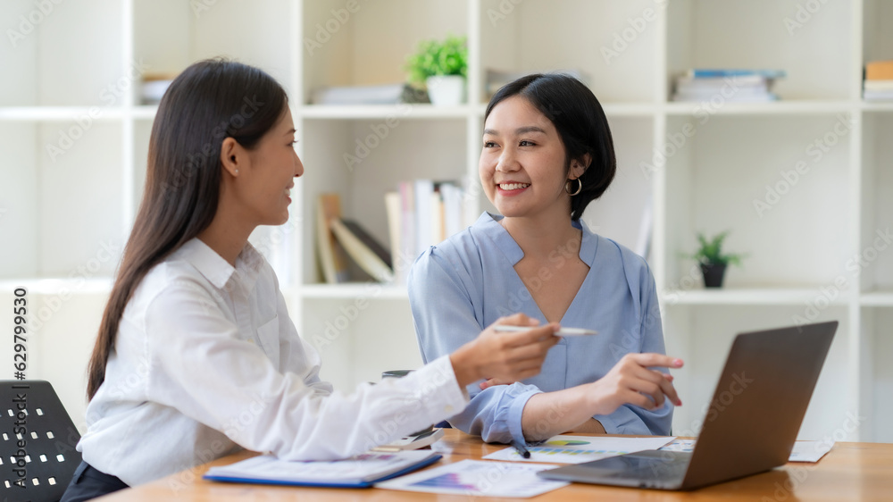 Two young Asian businesswoman consult and talk analysis of marketing planning with laptop computer.