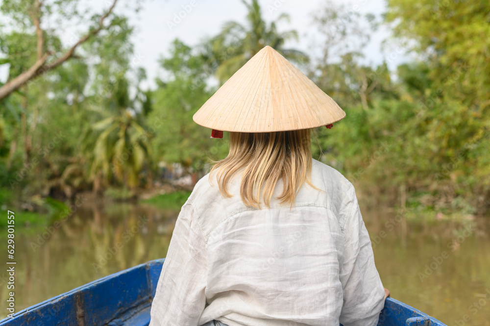 young traveler sitting on a boat and wearing a Vietnamese hat