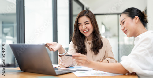 Happy young entrepreneurs smiling while working together in a modern workspace. Two young businesspeople sitting together at a table.