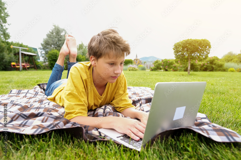 Foto de TTeen boy with a laptop sits in a park. School boy is typing on ...