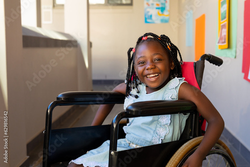 Portrait of happy african american schoolgirl sitting in wheelchair at elementary school corridor