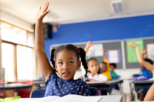 Canvas-taulu Diverse elementary schoolchildren sitting at desks and raising hands in class