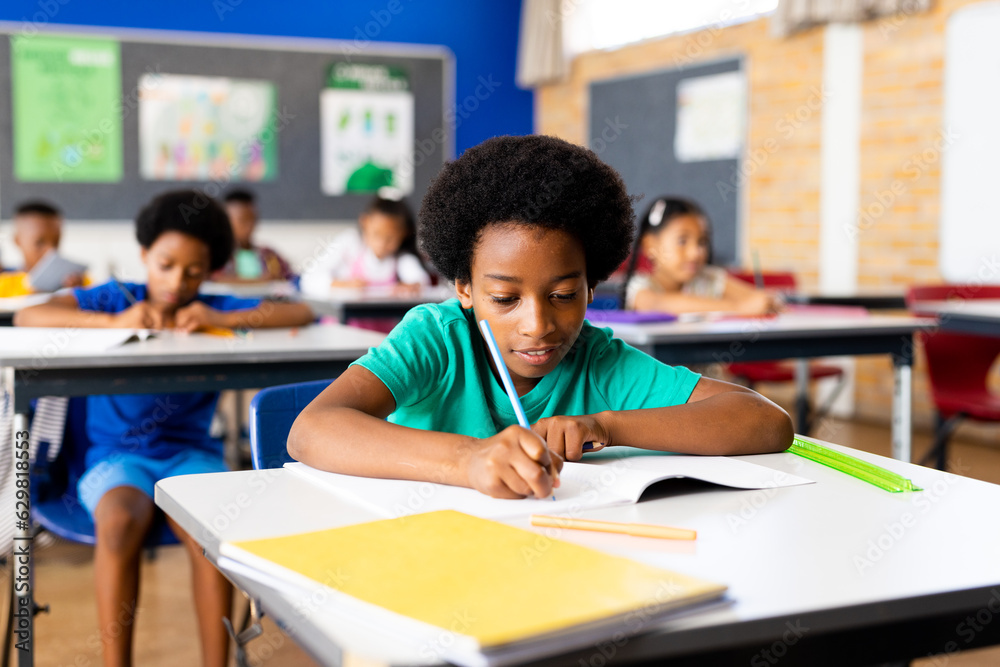 Portrait of happy african american elementary schoolboy writing in notebook at desk in class Portrait of happy african american elementary schoolboy writing in notebook at desk in class