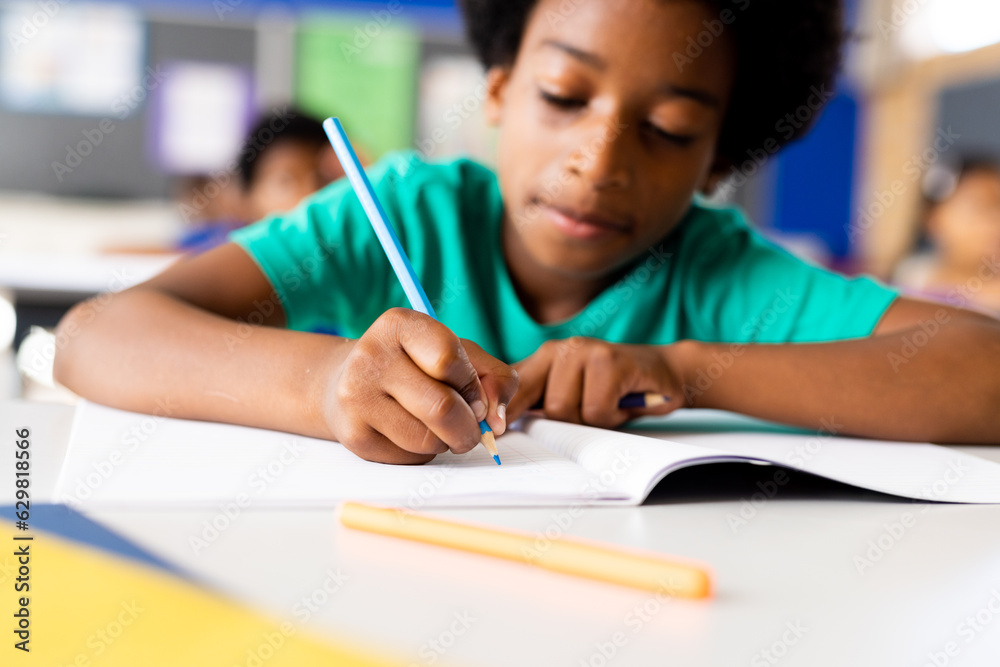 Portrait of happy african american elementary schoolboy writing in notebook at desk in class Portrait of happy african american elementary schoolboy writing in notebook at desk in class