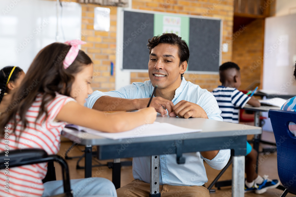 Happy biracial male teacher with girl in wheelchair in class at elementary school Happy biracial male teacher with girl in wheelchair in class at elementary school