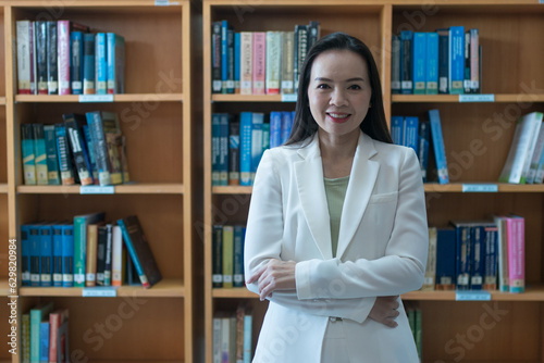 A female university lecturer in a business suit is searching for the book on the bookshelf in the library