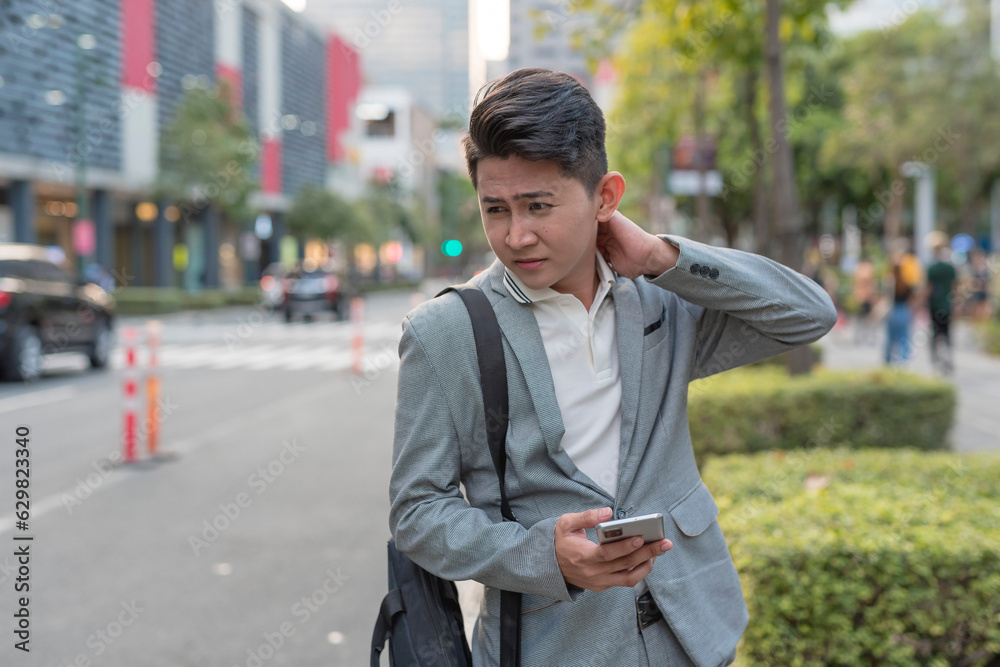 A young asian man suffers from a stiff neck from work while walking to a bus stop. Urban city setting. A young asian man suffers from a stiff neck from work while walking to a bus stop. Urban city setting.