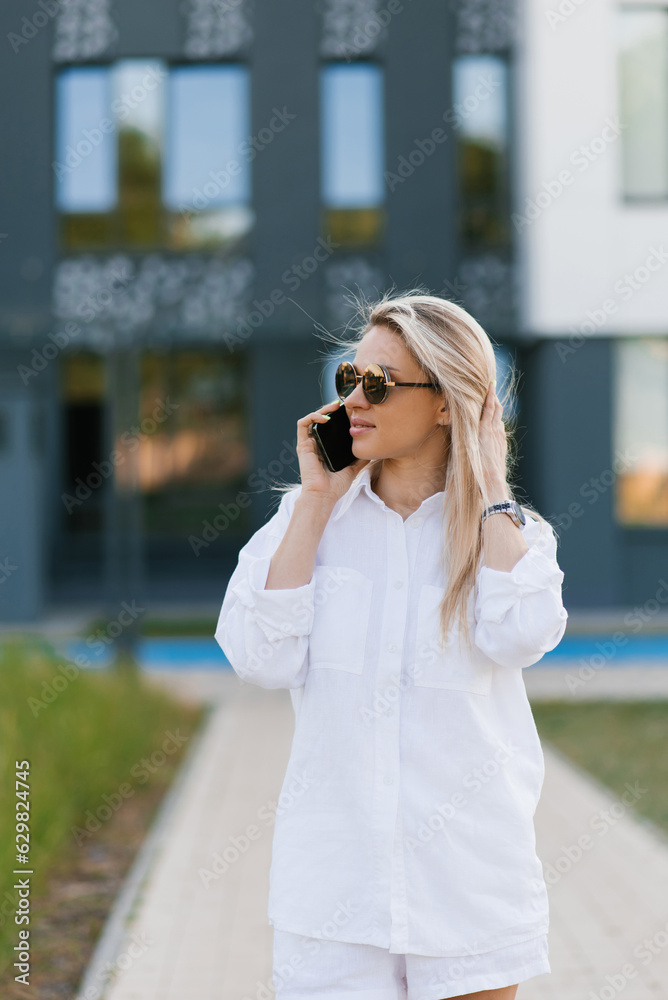 Side view portrait of a beautiful blonde woman holding a phone and laughing while talking on the phone against the background of the city. Side view portrait of a beautiful blonde woman holding a phone and laughing while talking on the phone against the background of the city.