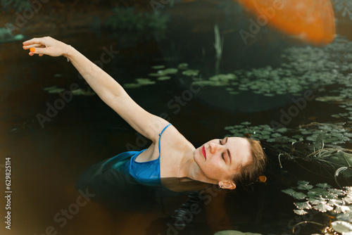 A beautiful blonde girl in a blue dress poses in a river with water lilies. The fairy tale of Ophelia. 