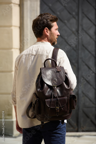 Handsome businessman walking on the street, with luxury leather dark brown backpack. Fashionable style.