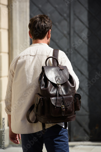 Handsome businessman walking on the street, with luxury leather dark brown backpack. Fashionable style.
