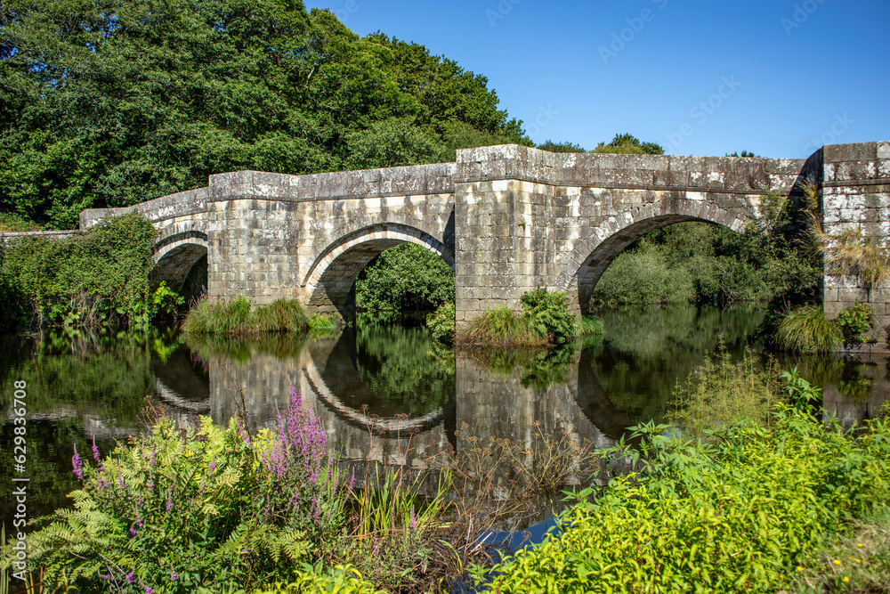 Fototapeta premium View of the Roman bridge of Brandomil, in A Coruna, Galicia, Spain, with its arches reflected in the calm waters of the river