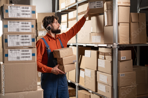Fotografía Male warehouse worker take box from shelf in big warehouse factory, Online shopp