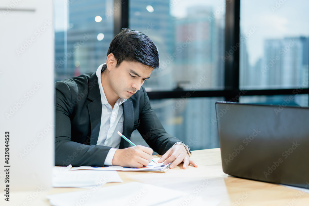 Handsome young businessman taking notes on paper at office The background is a blurred city. Handsome young businessman taking notes on paper at office The background is a blurred city.
