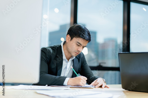 Handsome young businessman taking notes on paper at office The background is a blurred city.