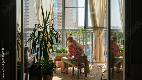 a woman grows and tends plants, strawberries on the balcony of a high-rise apartment building, back view