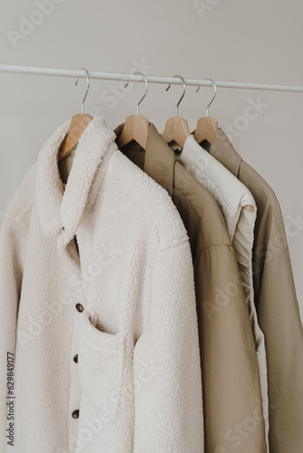 Autumn outerwear on hanger over white wall. Warm jackets, coats. Aesthetic wardrobe with clothes in neutral colours