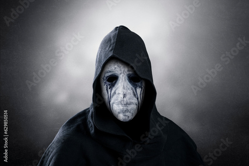 Spooky figure with hooded cape over dark misty background