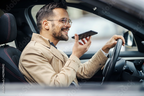 Tableau sur toile A happy young elegant man is driving his car and leaving a voice message on the phone