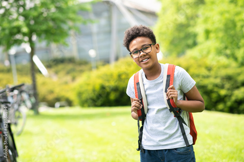 Schoolboy with backpack wearing white shirt standing in green park.