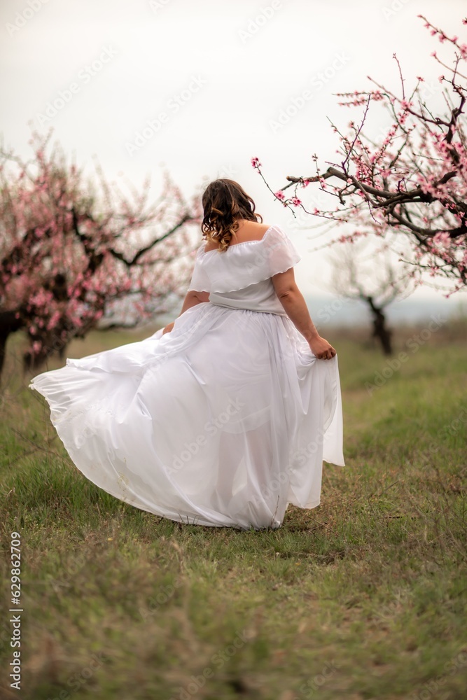Woman peach blossom. Happy woman in white dress walking in the garden of blossoming peach trees in spring Woman peach blossom. Happy woman in white dress walking in the garden of blossoming peach trees in spring