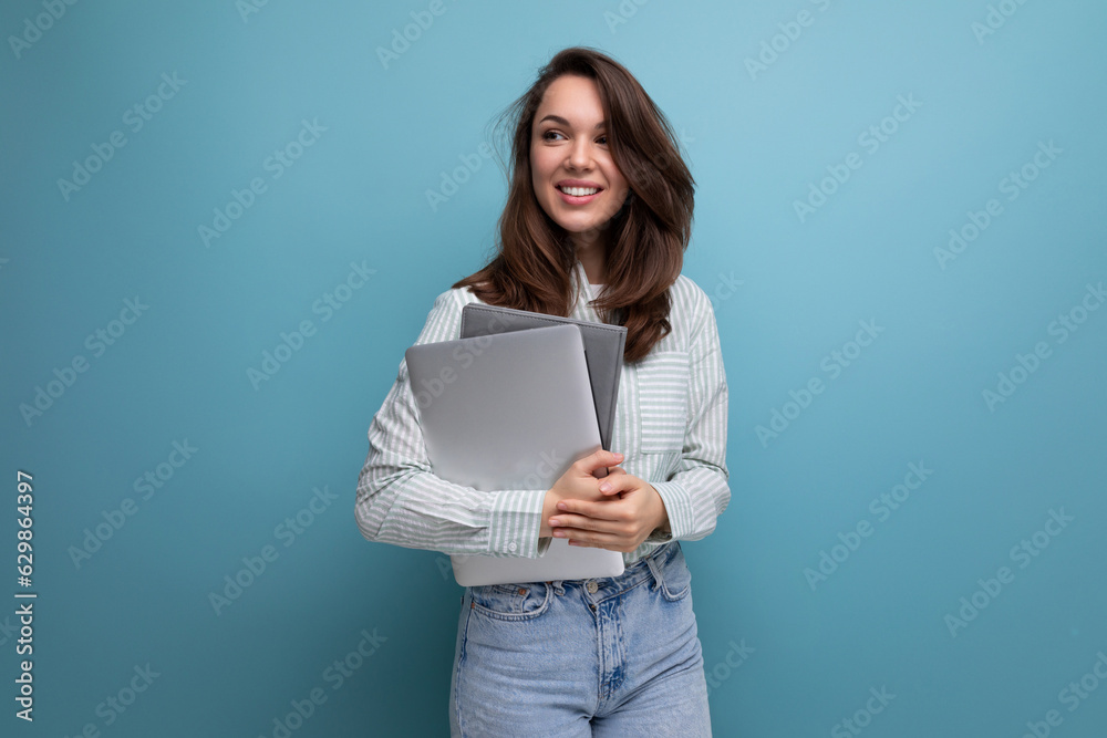 IT specialist 25 year old brunette woman in shirt and jeans enjoys freelancing holding a laptop in her hand IT specialist 25 year old brunette woman in shirt and jeans enjoys freelancing holding a laptop in her hand
