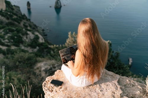Freelance women sea working on the computer. Good looking middle aged woman typing on a laptop keyboard outdoors with a beautiful sea view. The concept of remote work.