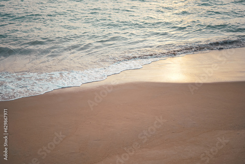 Ocean wave on sandy beach in twilight time background with sunlight reflection on wet sand. 