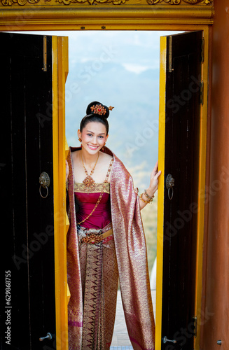 Beautiful Asian woman wear Thai traditional dress stand in area of ancient door of building look like temple and also look at camera with smiling.