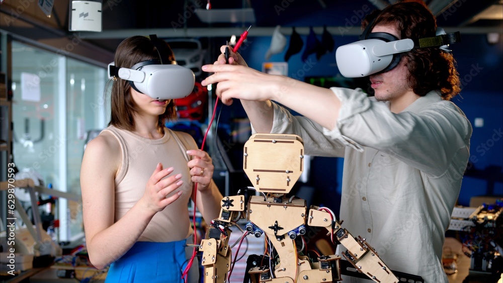 Two young engineers fixing a mechanical robot in the workshop, using VR virtual reality headsets